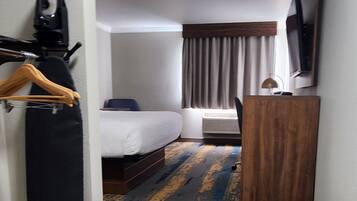 A hotel room with a bed, a desk, a TV, and a patterned carpet.