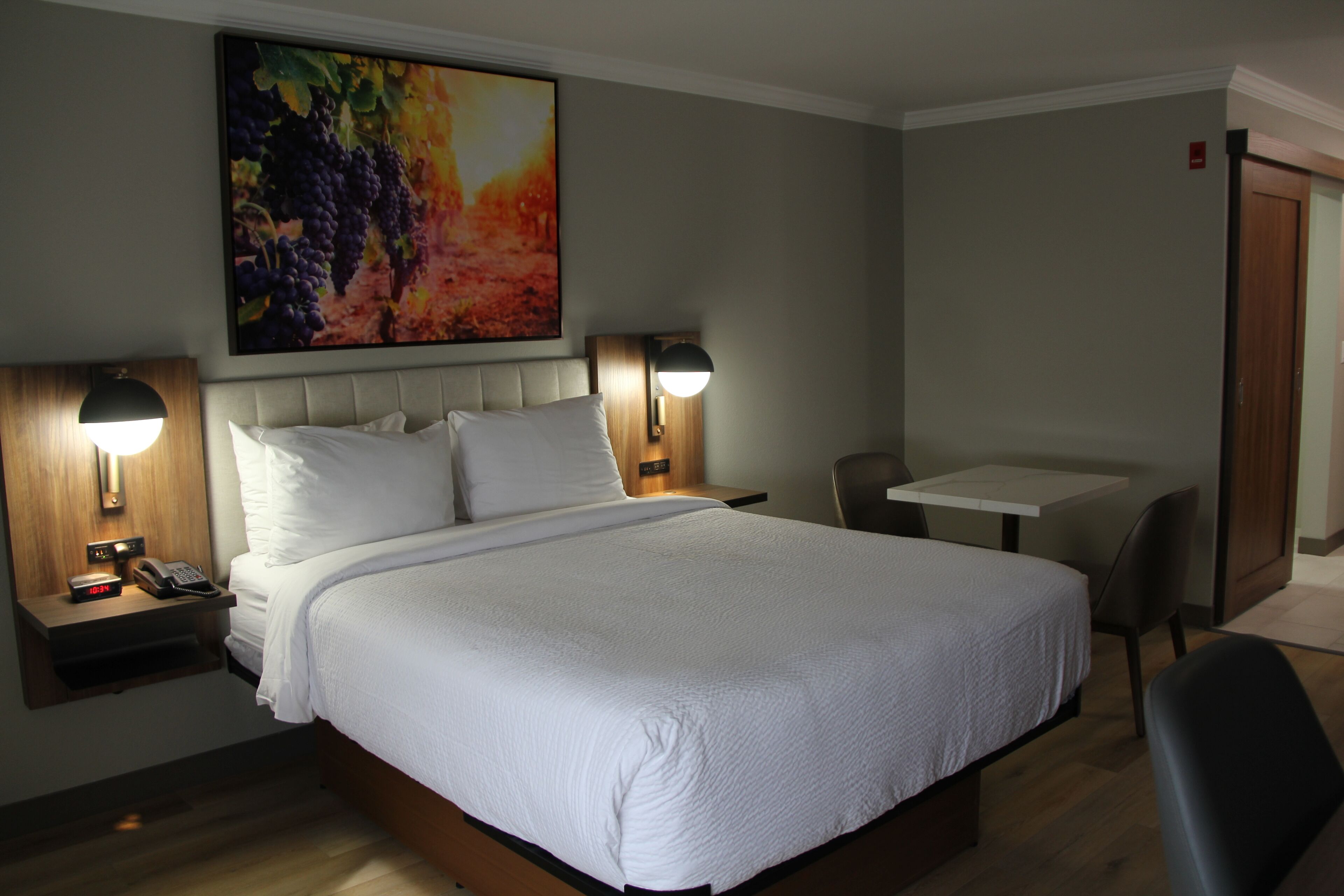 A hotel room with a large bed, two bedside lamps, a small table, and a chair.
