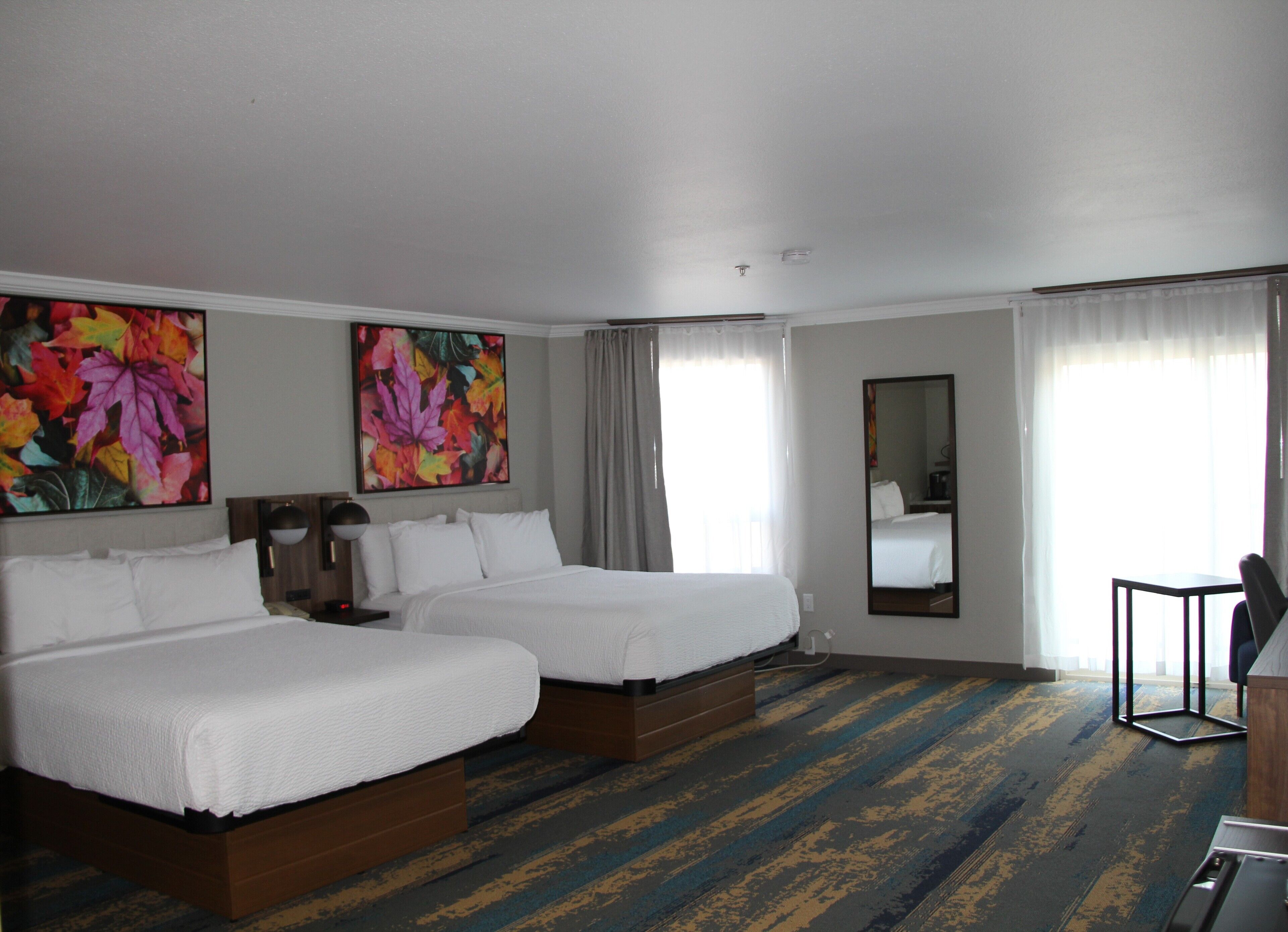 A hotel room with two beds, a large mirror, and a desk.