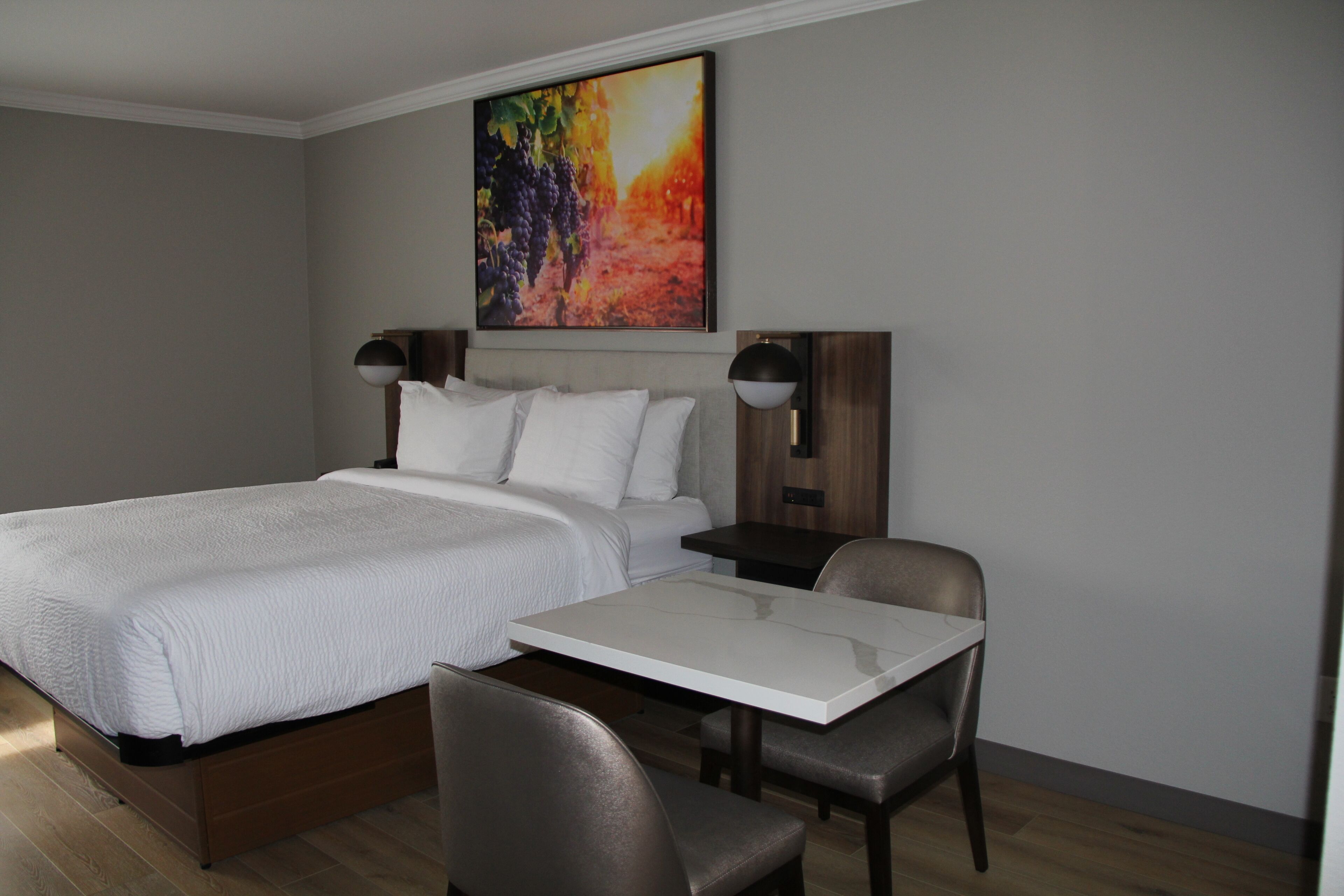 Een moderne hotelkamer met een groot bed, een eettafel, twee stoelen, een nachtkastje en een wandlamp.