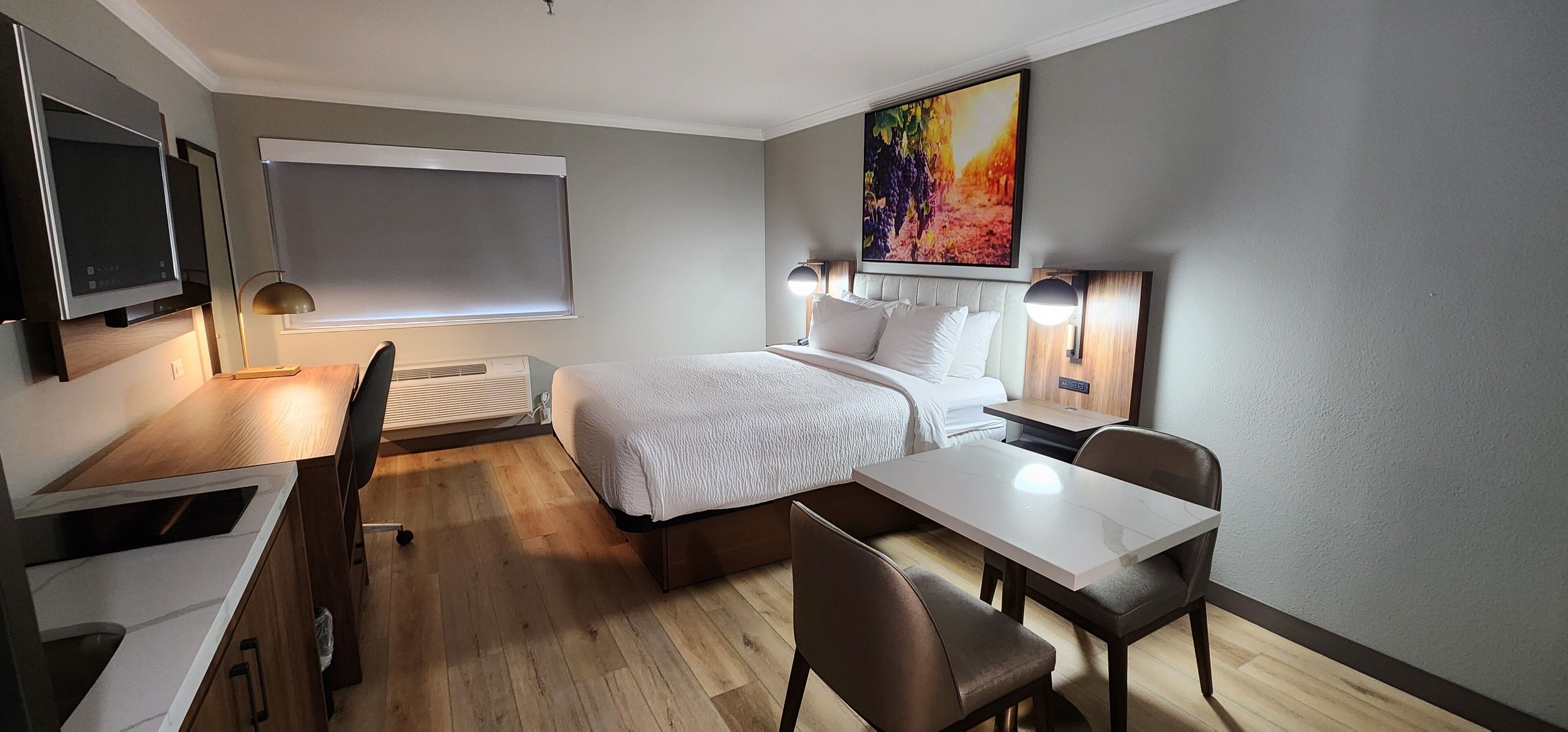Een hotelkamer met een bed, nachtkastjes, een bureau, een stoel, een televisie en een groot raam.