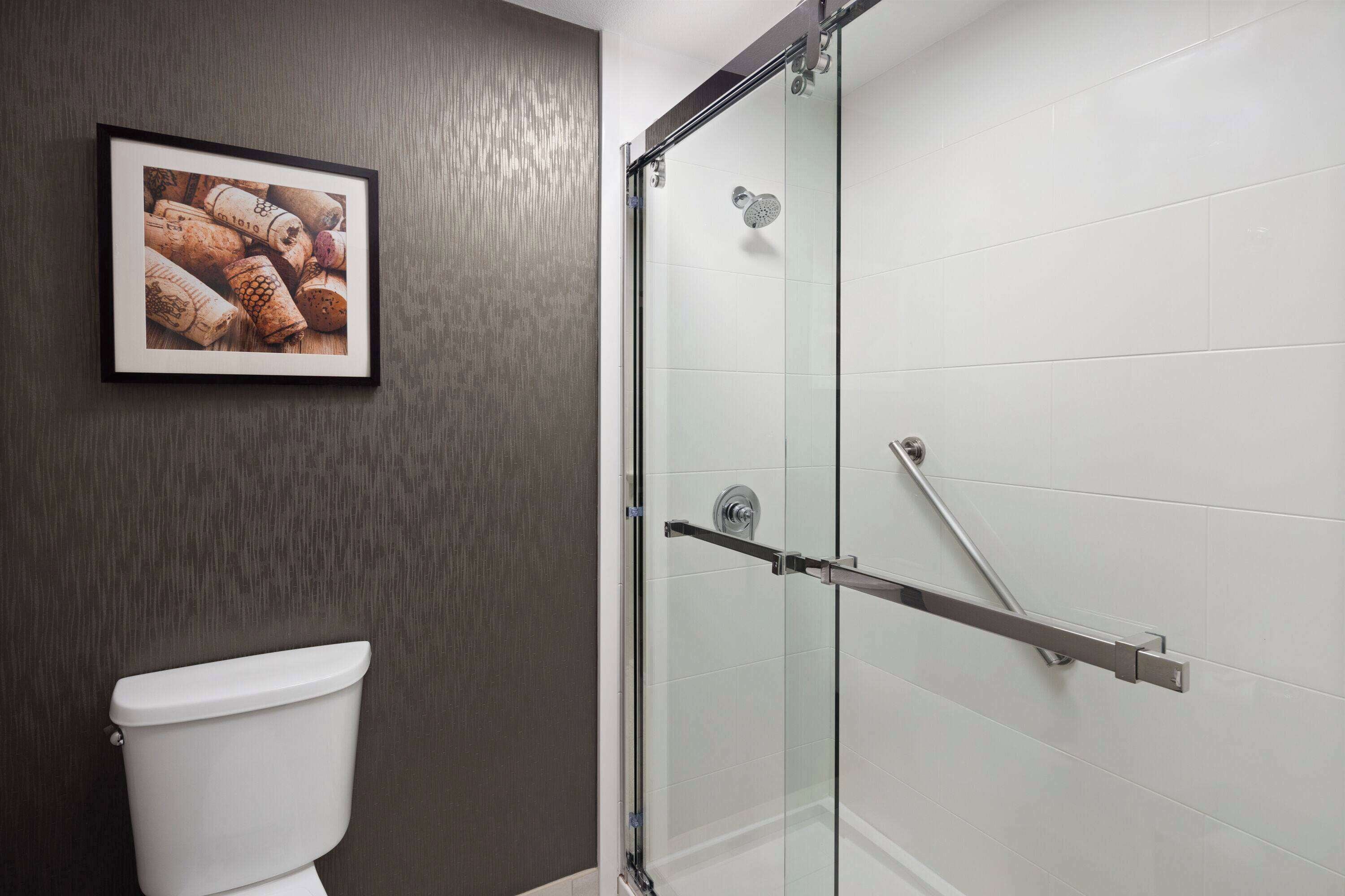 A bathroom with a glass shower enclosure, a framed picture of wine corks, and a white toilet.