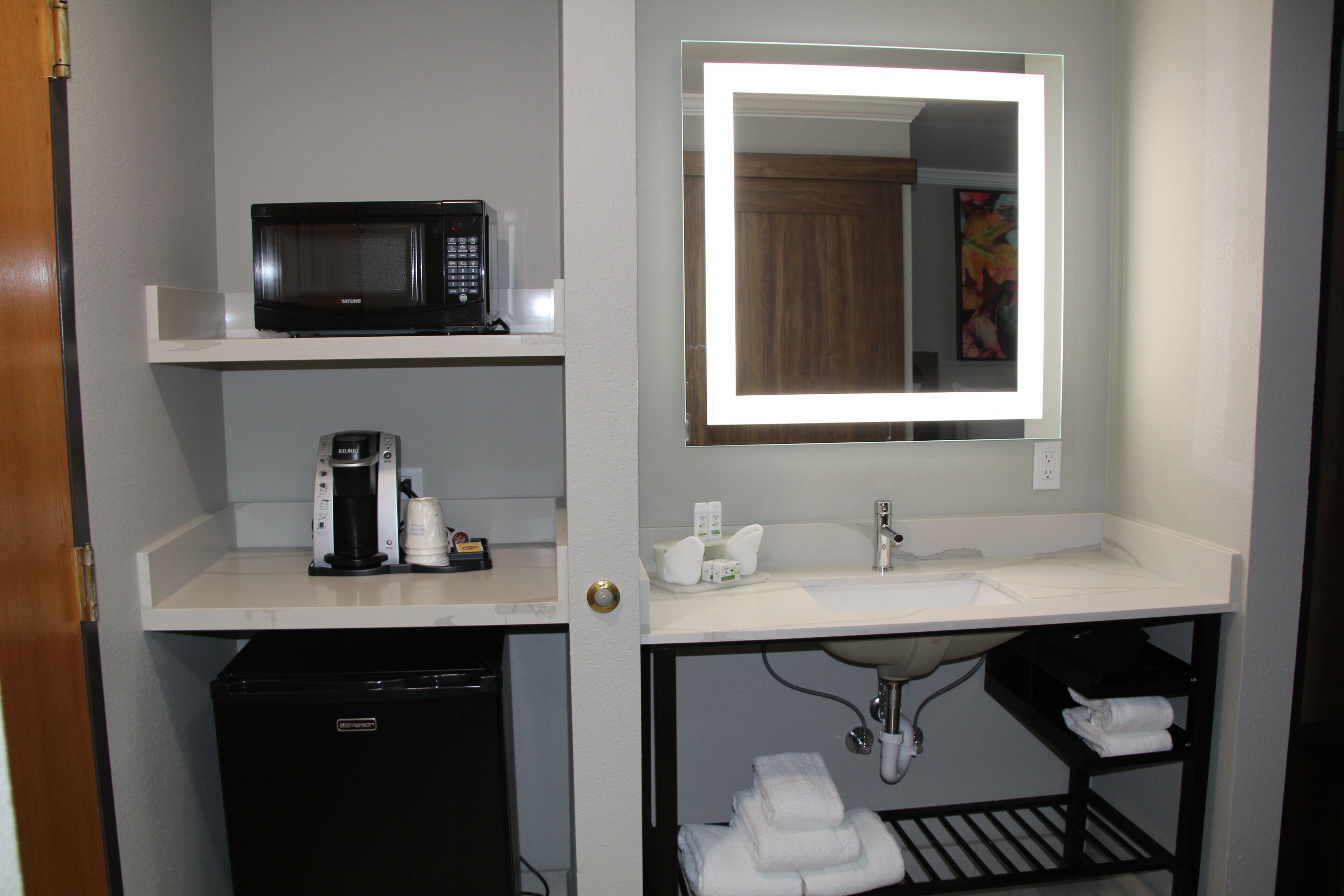 Une petite salle de bain d’hôtel équipée d’un four à micro-ondes, d’une machine à café, d’un lavabo et d’un miroir doté d’un cadre lumineux.