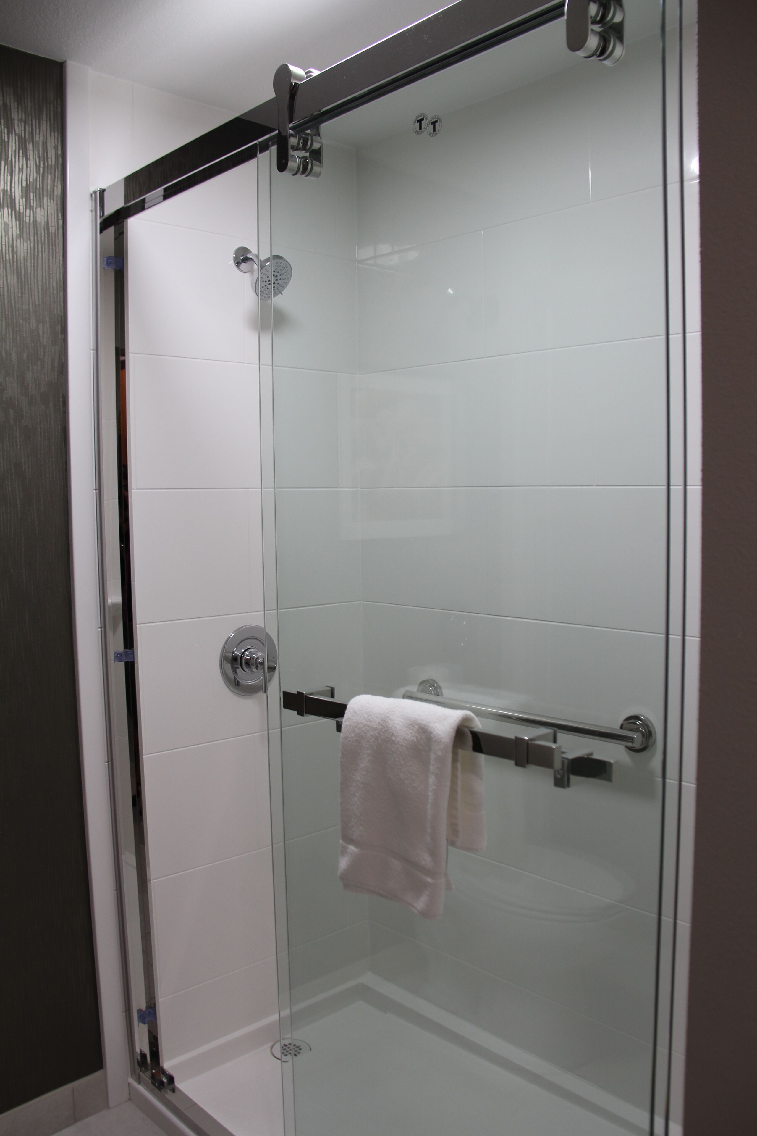 A glass-enclosed shower with a towel rack and a visible drain.