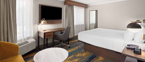 A hotel room with a bed, a desk, a chair, a small table, and a TV.