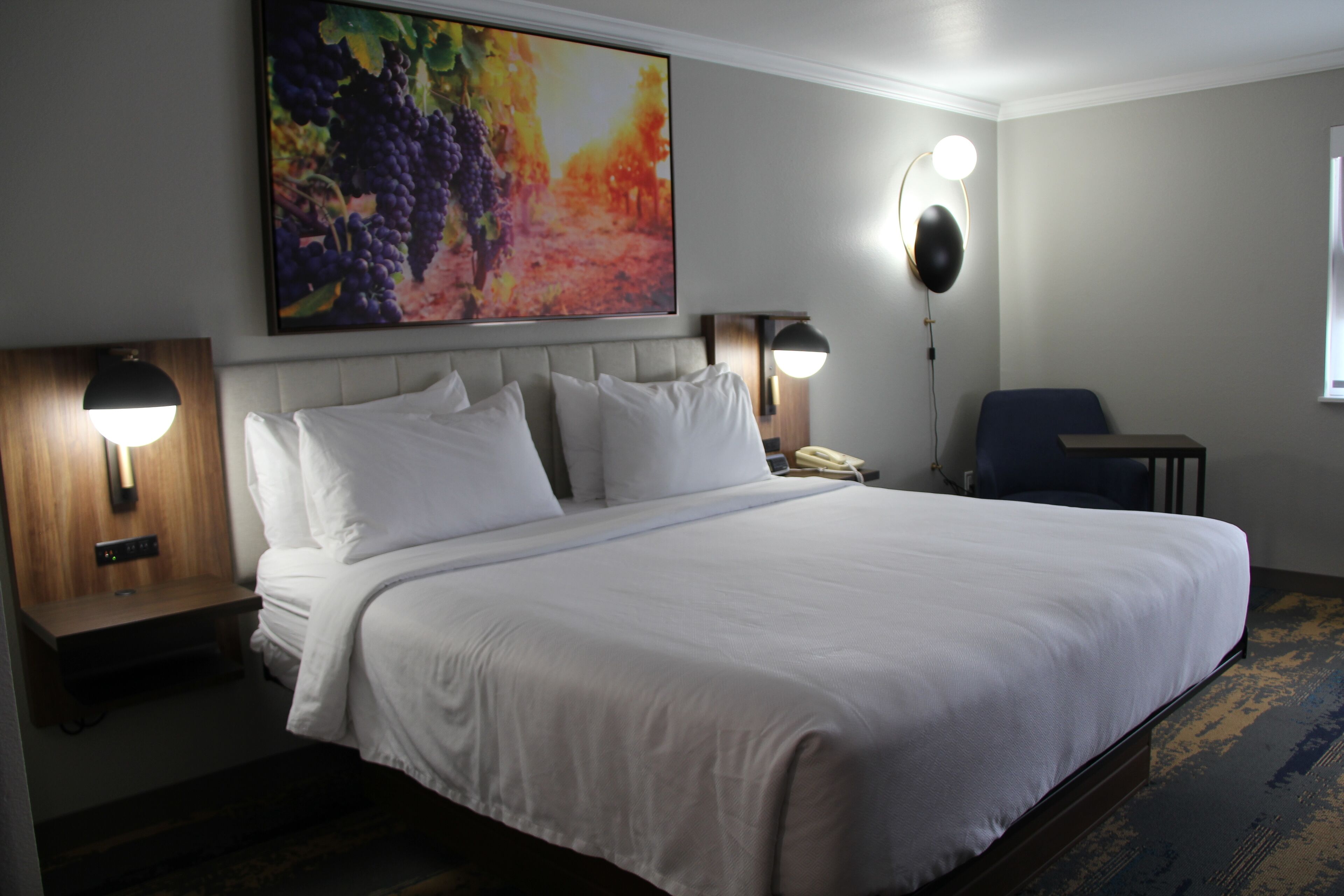 A hotel room with a large bed, two bedside tables with lamps, a desk, and a chair.