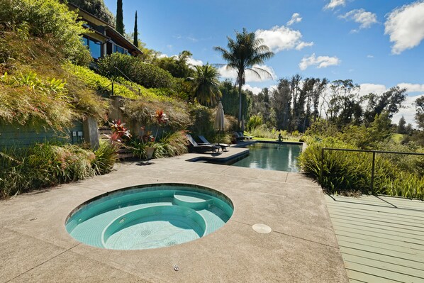 A swimming pool with a hot tub, surrounded by lush greenery and a wooden deck.