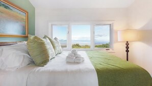 Habitación de hotel con cama, almohadas, una manta verde, una lámpara y un cuadro en la pared.