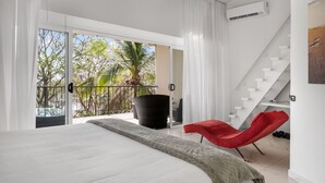 A modern bedroom with a large bed, a red chair, a balcony with a view of trees and a palm, and a staircase. - Beachfront Jewel in Langosta (tamarindo)