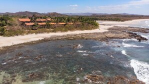 A coastal area with clear waters, a sandy beach, and a cluster of buildings with red roofs. - Beachfront Jewel in Langosta (tamarindo)