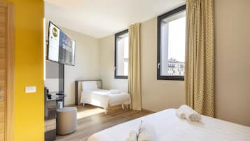 A hotel room with a bed, a desk, a chair, a small stool, and a window with curtains.