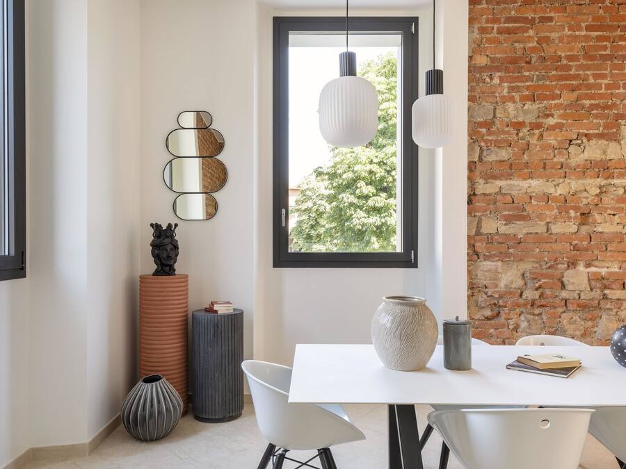 Uma área de refeições moderna com uma mesa branca, cadeiras pretas e uma parede de tijolos.