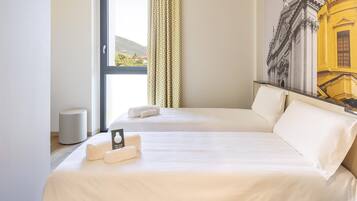 A hotel room with two beds, a large window, a painting of a building, and a small round table.