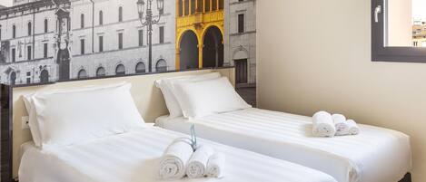 Habitación de hotel con dos camas, ropa blanca y toallas enrolladas.