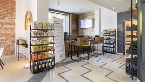 A modern interior with a brick wall, a counter with a menu board, and shelves stocked with snacks and beverages.