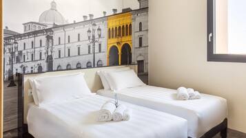 Une chambre d’hôtel avec deux lits, du linge de lit blanc et une fresque représentant un bâtiment historique.