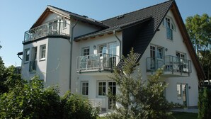 A two-story building with a balcony on the upper floor, a sloped roof, and a small front porch. - Dune house**** with use of swimming pool and sea view in top location ⭐️⭐️⭐️⭐️ (Göhren)