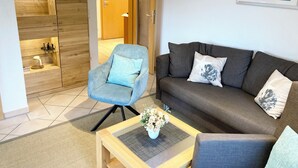 A modern living room with a grey sofa, a blue armchair, and a coffee table with a vase of flowers. - Dune house**** with use of swimming pool and sea view in top location ⭐️⭐️⭐️⭐️ (Göhren)