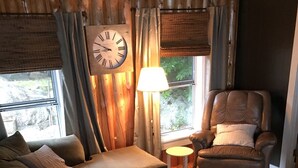 Un salon chaleureux avec un canapé en cuir marron, un fauteuil inclinable et une table basse en bois. On peut également apercevoir une grande horloge murale et une lampe.