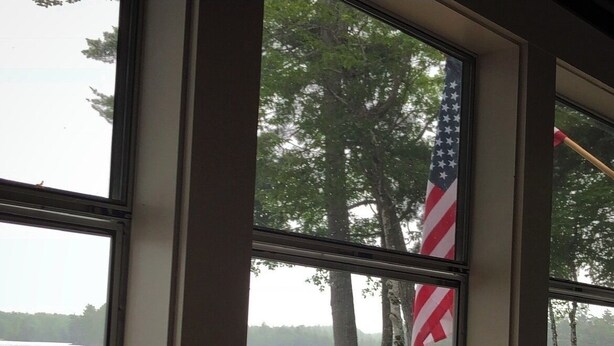Une vue par une fenêtre, avec une enseigne indiquant « MILLINOCKET, MAINE » et une bougie sur une table.