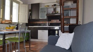 Une cuisine compacte dotée d’appareils électroménagers modernes, un coin repas avec une table et des chaises, et un canapé agrémenté d’un coussin.