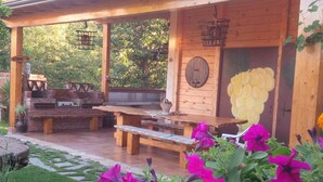 Un espace extérieur aménagé en terrasse, avec des bancs en bois, un barbecue et une porte en bois dotée d’une fenêtre circulaire.