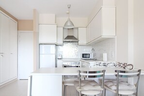 A modern kitchen with white cabinetry, a central island with chairs, a microwave, and a stainless steel range hood.