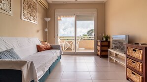 Et værelse med seng, fjernsyn, ventilator og en balkon med bord og stole.