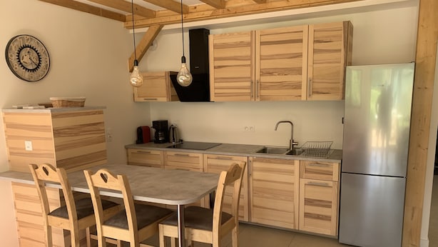 Une cuisine moderne avec des meubles en bois, un réfrigérateur en acier inoxydable et un coin repas avec des chaises en bois.