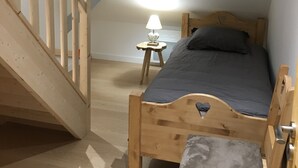 Une chambre avec un plafond en pente, un lit en bois, une table de chevet avec une lampe et une fenêtre donnant sur les montagnes.