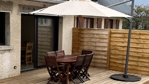 Une terrasse en bois avec une table et des chaises, un parasol blanc et une clôture en bois.