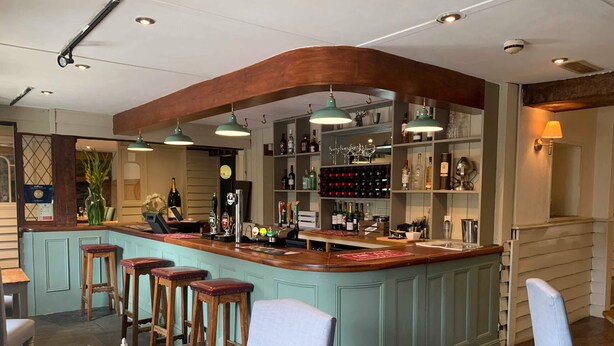 Eine Bar mit einer gebogenen Holztheke, mehreren Hockern und mit Flaschen gefüllten Regalen.