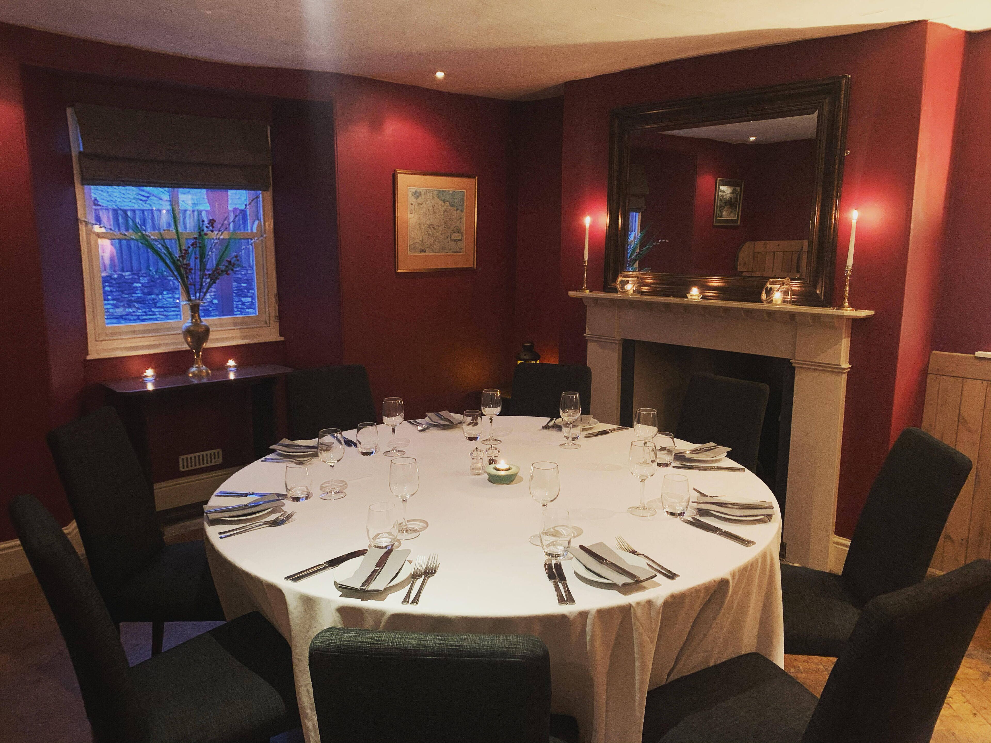 Une salle à manger avec une table ronde dressée pour le repas, des chaises disposées autour de la table, une fenêtre donnant sur un beau paysage et une cheminée.