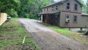 A two-story house with a porch, a dirt driveway, and a car parked in the background. - Private cottage on Susquehanna river Very private !! (Berwick)