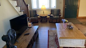 A living room with a wooden staircase, two armchairs, a coffee table, a TV, a fan, and a door. - Private cottage on Susquehanna river Very private !! (Berwick)