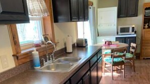 A compact kitchen with dark cabinets, a stainless steel sink, a microwave, and a dining area with a table and chairs. - Private cottage on Susquehanna river Very private !! (Berwick)