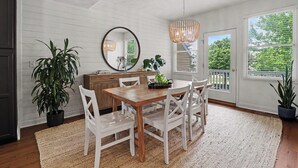Un coin repas avec une table en bois, des chaises blanches, un lustre et des plantes en pot.