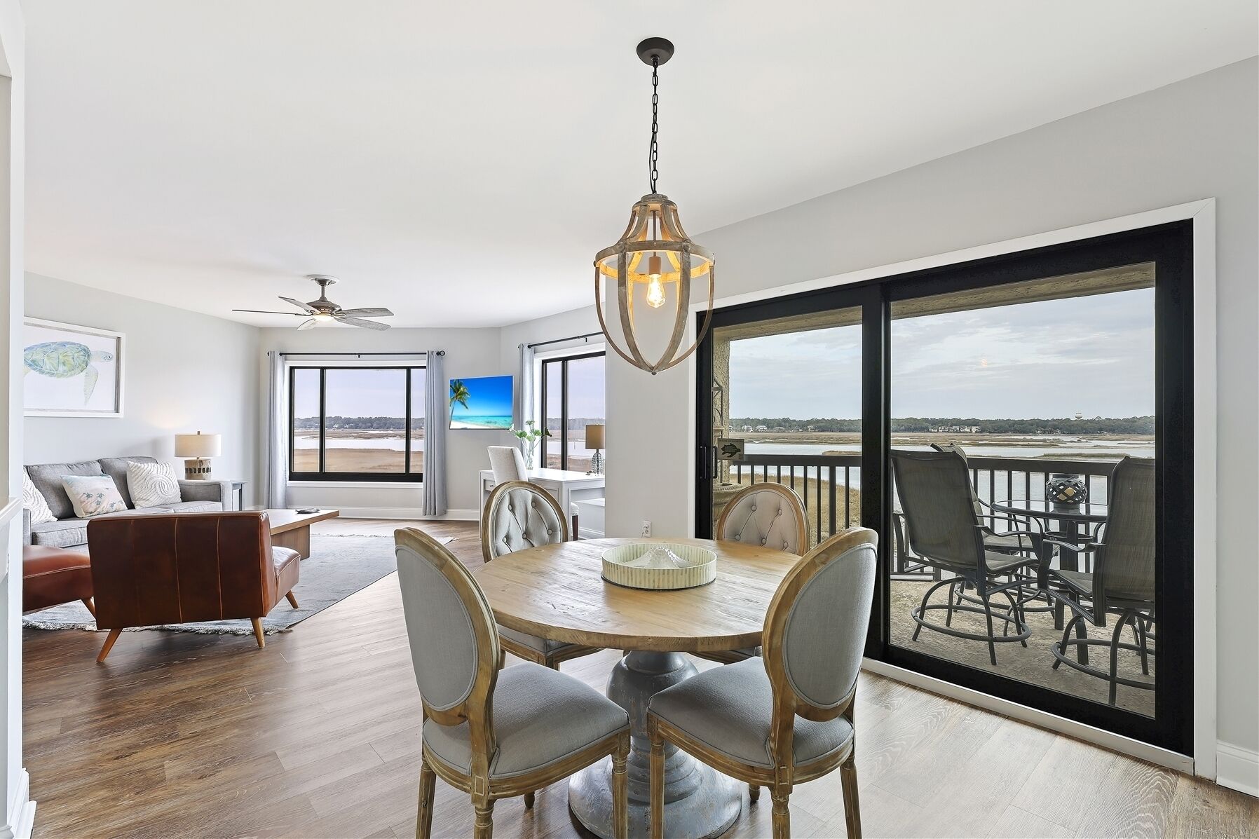 A spacious living room with a dining area, large windows, and a view of the beach.