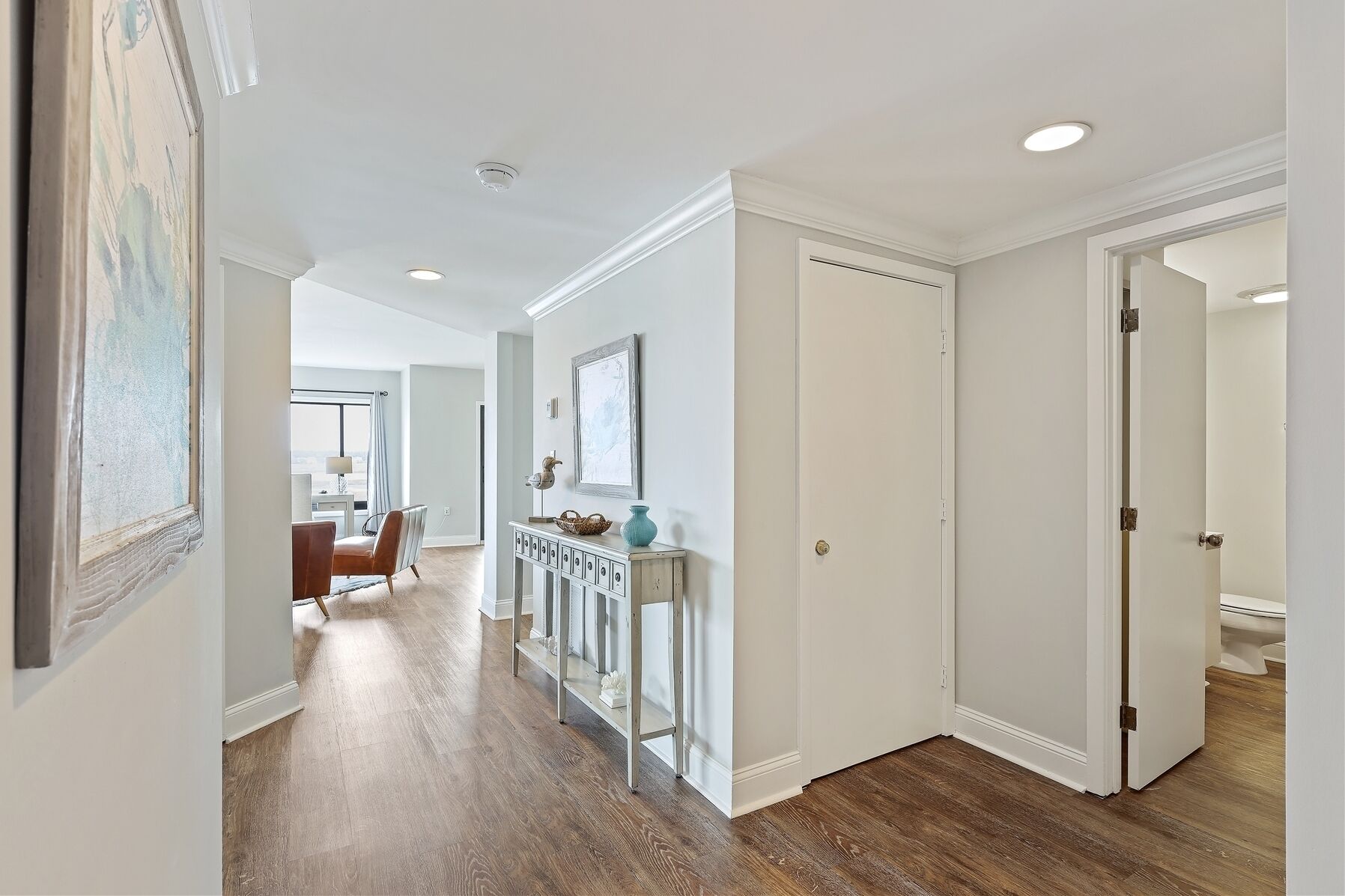 A hallway with a wooden floor, white walls, and a door leading to a bathroom.