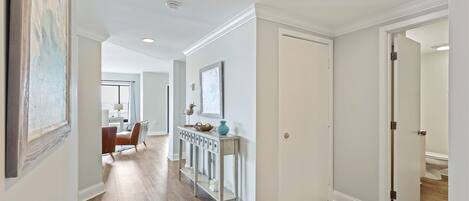 A hallway with a wooden floor, white walls, and a door leading to a bathroom.