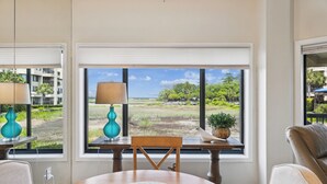 A room with a round table, two chairs, a lamp, and a view of a landscape through large windows.