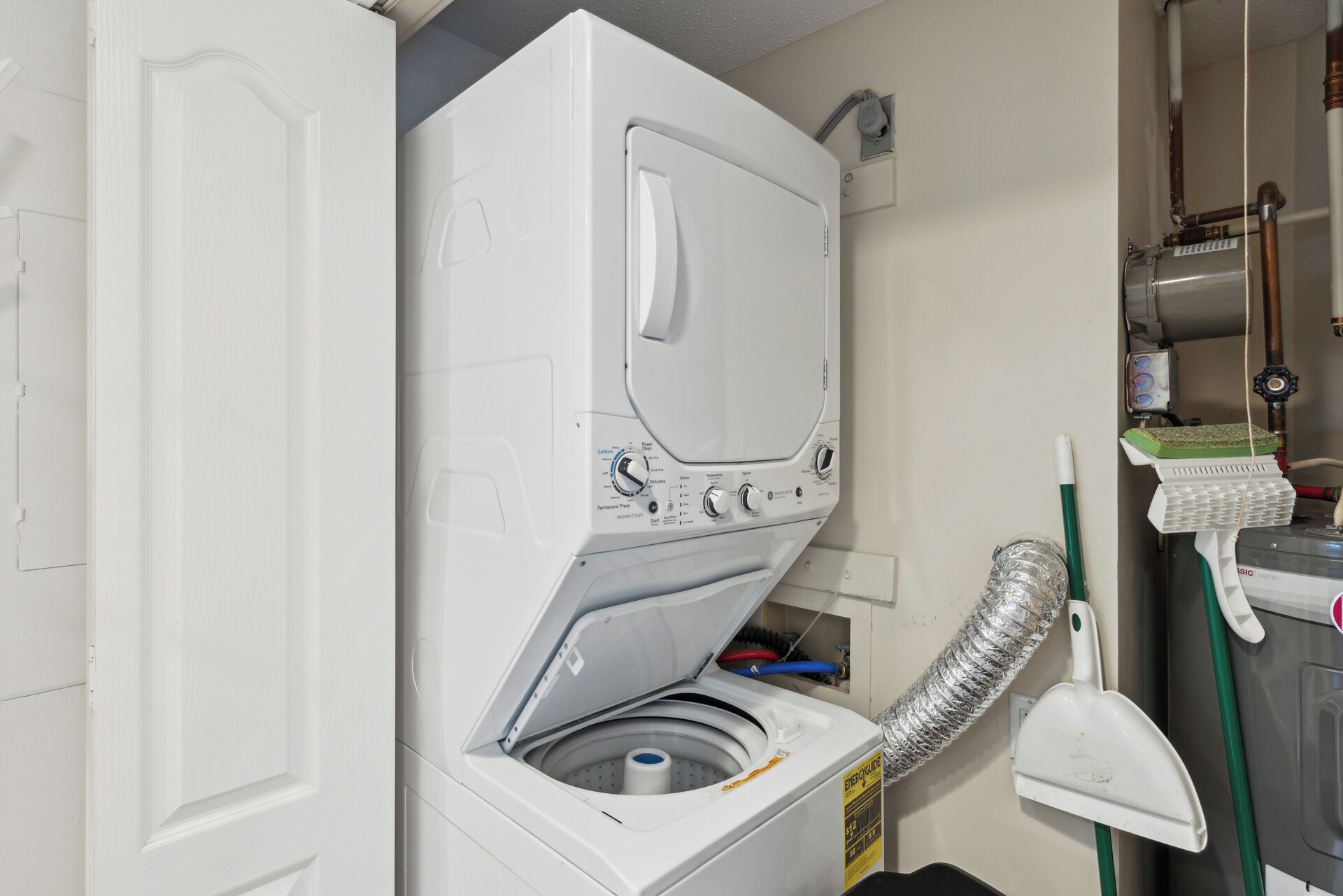 Een kleine wasruimte met een voorlader wasmachine, een slang en een bezem.