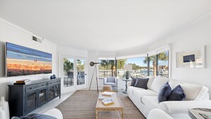 A modern living room with a large painting, a sofa, a coffee table, and a view of the outdoors. - Beautiful Water & Marina Views, Bike to Beach! (Hilton Head Island)
