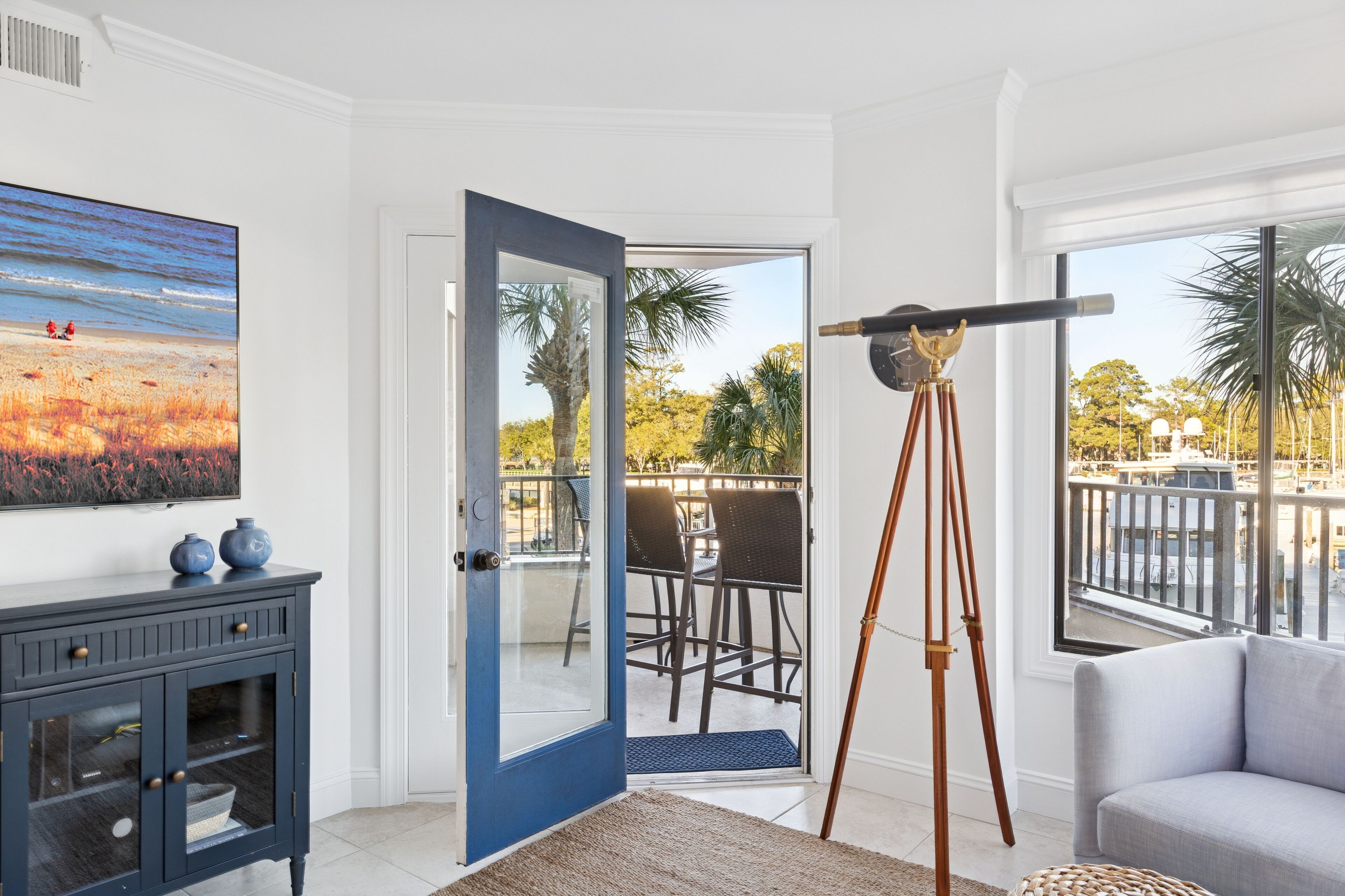 A room with a large window, a telescope, a painting, and a dark blue cabinet.