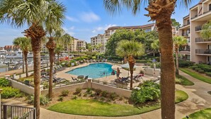 A pool area with lounge chairs, palm trees, and a view of a marina. - Beautiful Water & Marina Views, Bike to Beach! (Hilton Head Island)