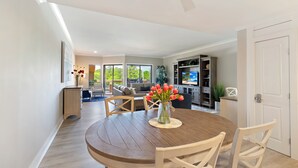 A dining area with a round wooden table, white chairs, and a vase of red flowers. - Water & Marina Views, Pet Friendly-Near Beach (Hilton Head Island)