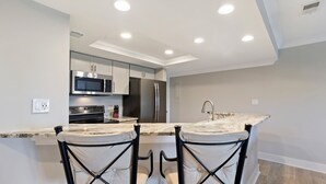 A modern kitchen with stainless steel appliances, a marble countertop, and two upholstered bar stools. - Water & Marina Views, Pet Friendly-Near Beach (Hilton Head Island)