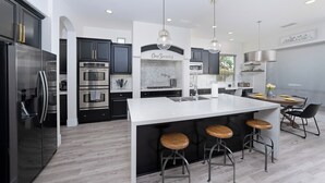 Una cocina moderna con una isla central, taburetes de bar, electrodomésticos de acero inoxidable y un comedor con una mesa redonda y sillas.