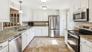 A modern kitchen with white cabinets, stainless steel appliances, granite countertops, and a tiled floor. - Pet Friendly with Scenic Views, Close to Beach! (Hilton Head Island)