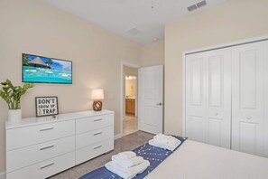 A hotel room with a bed, a TV mounted on the wall, a white dresser, and a door leading to a bathroom. - Lake View and Mickey Room! Stunning Home! #5sl851 (Kissimmee)
